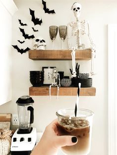 a person holding a drink in front of a wall with halloween decorations and skeletons on it