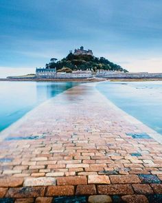 a brick walkway leading to an island in the middle of the ocean with a castle on top