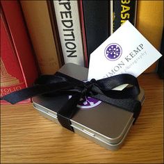 a small metal box with a black ribbon tied around it and some books in the background