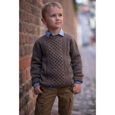 a young boy standing next to a brick wall wearing a brown sweater and khaki pants