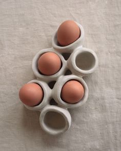 four eggs are arranged in the shape of egg cups on a white tablecloth surface