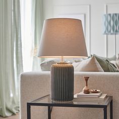 a table lamp sitting on top of a glass table next to a couch in a living room