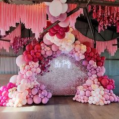 balloons and streamers are hanging from the ceiling in an indoor space that is decorated with pink