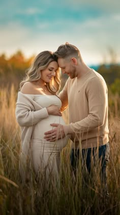 a pregnant couple standing in tall grass at sunset