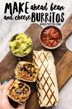 a person holding a burrito on a cutting board with salsa and guacamole