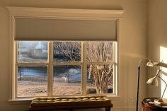 an empty room with a bench, lamp and window in the corner that looks out onto a yard