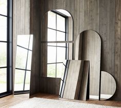 an assortment of mirrors in front of two windows on a wooden floor next to a rug