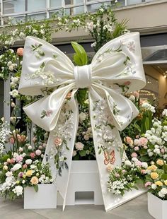 a large white bow on top of some flower potted plants in front of a building