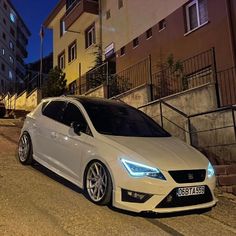 a white car parked on the side of a road next to tall buildings at night