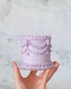 a hand holding a purple cake on top of a marble counter