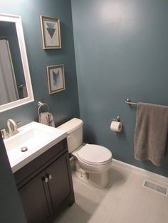 a white toilet sitting next to a sink in a bathroom under two framed pictures on the wall