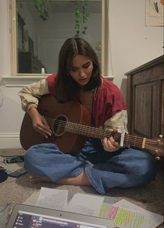 a woman sitting on the floor playing an acoustic guitar