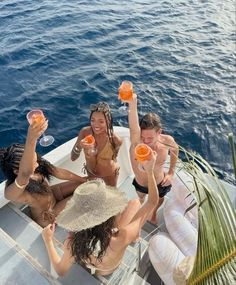 four people sitting on a boat with drinks in their hands and one person holding an orange