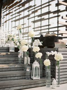 white flowers in vases are lined up on the steps to an outdoor wedding ceremony