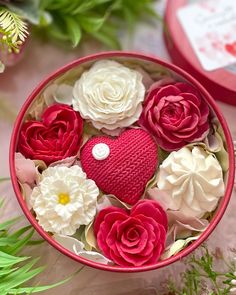 red and white flowers in a pink box with a heart on the top, surrounded by greenery