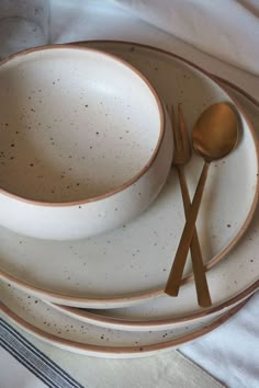 a white plate topped with two gold colored spoons next to a brown and white bowl