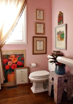 a white toilet sitting next to a window in a pink walled room with pictures on the wall