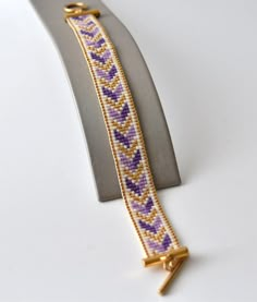 a yellow and purple beaded bracelet sitting on top of a silver display stand next to a white wall