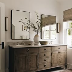 a bathroom with two large mirrors above the sink and a vase filled with flowers in front of it