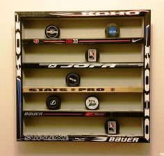 a display case with hockey stickers and puck caps on the bottom shelf in front of a white wall