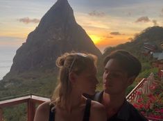 a man and woman looking at each other in front of a mountain