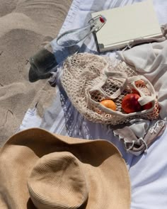 a hat, book and other items on a blanket at the beach in the sand