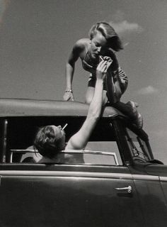 a woman is sitting on the hood of a car while holding onto a man's leg