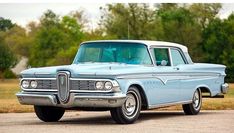 an old blue car is parked on the side of the road with trees in the background