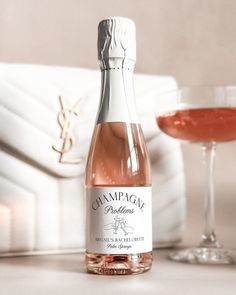 a bottle of champagne sitting next to a glass filled with pink liquid and a white purse