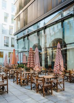 tables and chairs are lined up outside in front of a building with striped umbrellas on them