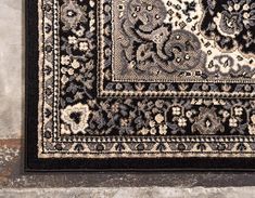 a black and white area rug with an ornate design on the bottom, in front of a stone wall