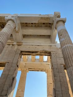 looking up at the columns and roof of an ancient building with blue skies in the background