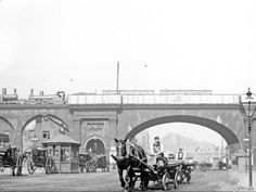 an old black and white photo of horse drawn carriages in front of a stone bridge