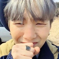 a young boy wearing a hat and holding his hand up to his mouth while smiling at the camera