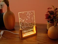 a wooden table topped with a light up sign and vase filled with flowers next to it