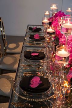 a long table is set with black and pink plates, silverware, and candles