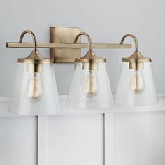 three light bathroom fixture with clear glass shades and brass finish on the wall behind it