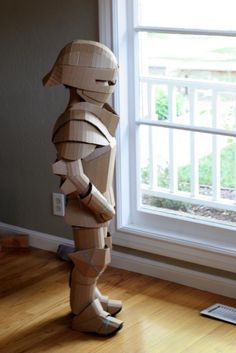 a cardboard robot standing in front of a window next to a book on the floor