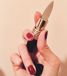 a woman's hand holding a lipstick and a knife