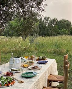 an outdoor table with plates and bowls of food on it in the middle of a field