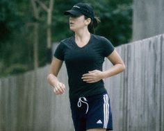 a woman running down the street wearing a black shirt and blue shorts with white stripes