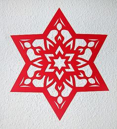 a paper cut snowflake on a white wall in the shape of a star