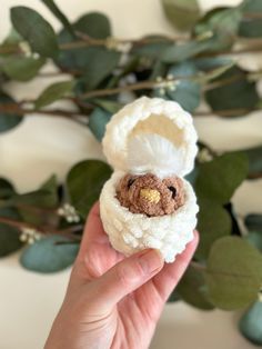 a hand holding a small teddy bear in a white crochet hat and coat