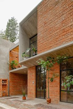 a brick building with large windows and plants in pots on the outside wall, next to an entry way