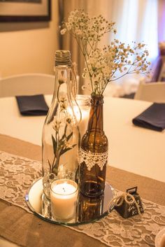 two bottles with flowers and candles on a table