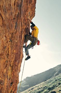 a man climbing up the side of a mountain with his hands in the air while holding onto a rope