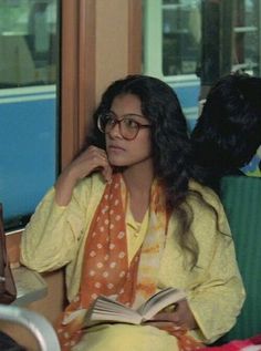 a woman sitting on a train with a book in her hand and looking out the window