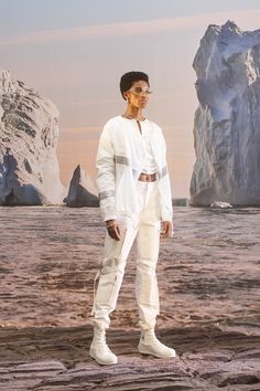 a man standing in front of an iceberg with his hands on his hips and wearing white pants