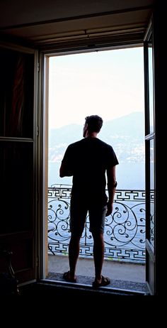 a man standing in front of an open door looking out at the mountains and water