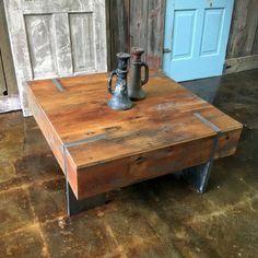 an old wooden table with a metal coffee pot on it's top, sitting in front of a blue door